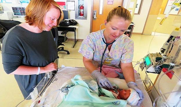 NICU nurse checking breathing and heart rate of premature baby, while new mom watches on. (Source: Health.mil)